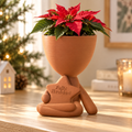Matera terracota con forma de hombrecito sentado y estrella Feliz Navidad en ambiente navideño.