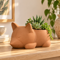 Portamaceta decorativo con forma de cachorro dormilón en color terracota, ambientado con plantas en un espacio cálido